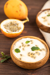 Yoghurt with granadilla and mint in wooden bowl on brown wooden, side view, selective focus.
