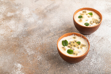 Yoghurt with granadilla and mint in clay bowl on brown concrete, side view, copy space.