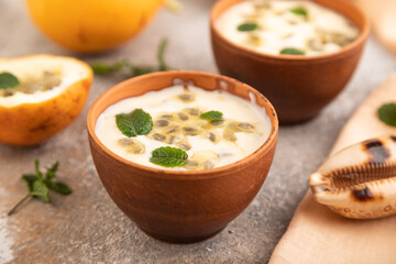 Yoghurt with granadilla and mint in clay bowl on brown concrete, side view, selective focus