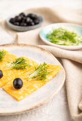 Marble cheese with olives and watercress microgreen on gray concrete. side view, selective focus.