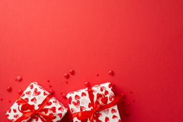 Valentine's Day concept. Top view photo of present boxes and heart shaped sprinkles on isolated red background with empty space