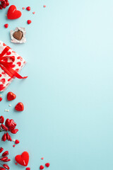 Valentine's Day concept. Top view vertical photo of giftbox with ribbon bow heart shaped chocolate candies candles and sprinkles on isolated light blue background with copyspace