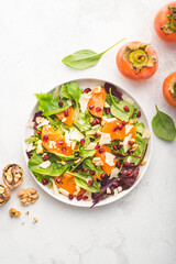 Juicy unusual salad with persimmon, pomegranate, fresh spinach, various leaves, pecorino cheese and walnuts. Sweet and salty tastes, winter and autumn salads, gluten free recipe
