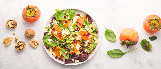 Juicy unusual salad with persimmon, pomegranate, fresh spinach, various leaves, pecorino cheese and walnuts. Sweet and salty tastes, winter and autumn salads, gluten free recipe. Internet banner