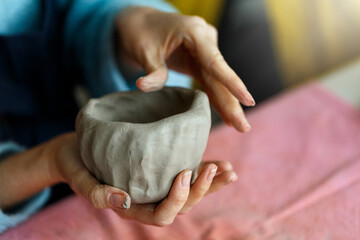 Women's hands knead the clay and sculpt a cup or bowl from it. The process of manufacturing a...