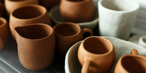 A close-up of various drying clay tableware on a shelf. A pottery studio concept. Craftmade dishes, bowls, pots, mugs of different colors. Cozy view. workshop with ceramic dishware