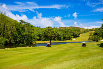 Golfers drive a golf car across a golf course in the Seychelles. Golf sport in the background of a...