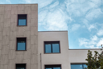 Modern residential building facade architecture details. Tiled and white walls with blue windows on cloudy sky, real estate outdoor design elements