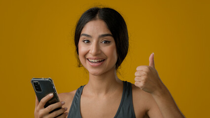 Happy Indian ethnic woman girl lady female smile browsing cell smartphone looking at camera with recommendation gesture swipe in mobile phone showing thumb up approve online bet winning super app