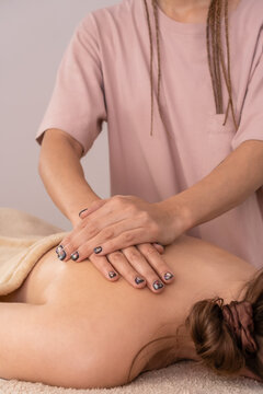 Female masseur massages the back and shoulder blades of a young brown-haired woman in a spa with soft lighting, close-up.Concept of body care, health, massage spa treatments.Vertically photo