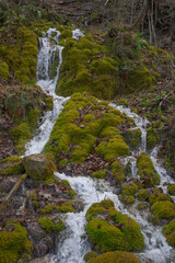 The water flows from the mountain slopes, between the rocks covered with moss.
