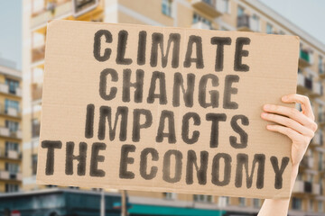 The phrase " Climate Change Impacts the Economy " is on a banner in men's hands with blurred background. Destruction. Crisis. Cost. Chemical. Global Warming. Protection. Oil. Money. Price. Petroleum