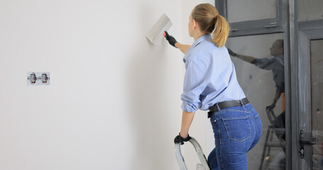 Woman puts putty on the walls with a wide spatula