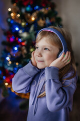Obraz na płótnie Canvas a girl listens to music with headphones in front of a Christmas tree in a purple suit
