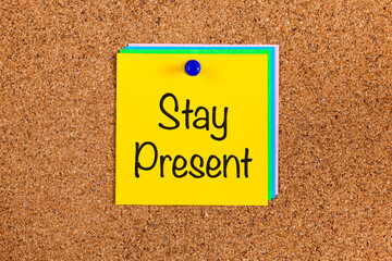 Note with words Stay Present on a corkboard