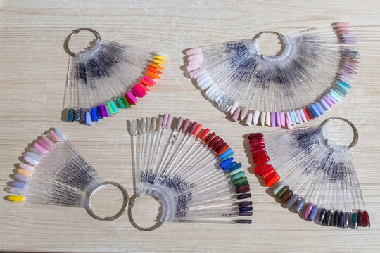 Fan-shaped tips with gel polish nail art samples with metal rings. Palettes of different shades of colors for manicure design on light wooden table top view