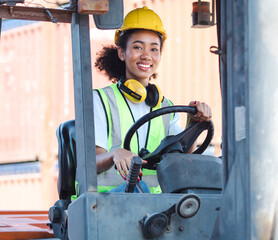 Young female foreman employee driving forklift at shipping container yard, portrait. Afro multiracial industrial engineer woman in safety vest drives reach stacker to lift cargo box at logistic dock