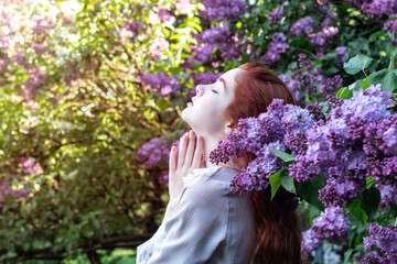 Fototapeta premium young girl with long red hair with lilac flowers in the garden in spring