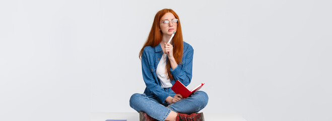Concentrated, thoughtful and creative young female genius with red hair, in glasses, looking...