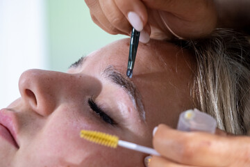 Hands of makeup artist apply means for laminating eyebrows with brushes. Professional lamination...