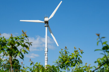 Konzept grüne Energie: Riesiges weißes Windrad und blauer Himmel mit Sträuchern, Zweigen und...