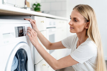 young woman turn on washing machine at home - obrazy, fototapety, plakaty