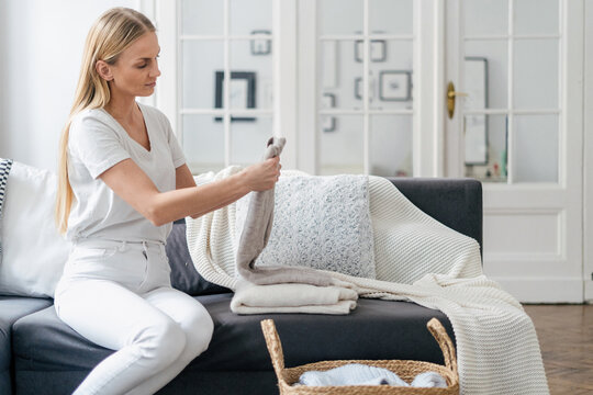 Young Woman Folding Clean Clothes On Couch At Home