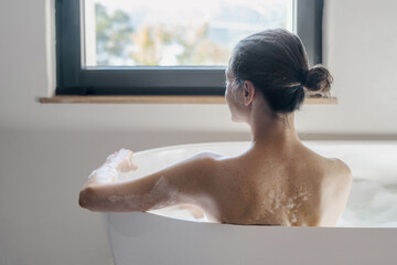 Female sitting in bath with bubbles, looking at window