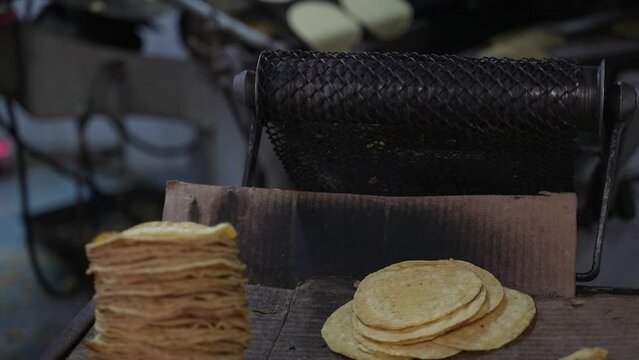 Closeup of freshly made tortillas flopping off the conveyor belt as a hand picks them up.