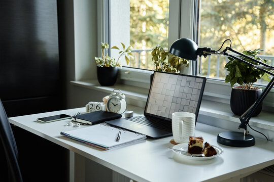 Home office workplace with laptop, documents and cup of tea placed on table in front of window. Remote work concept