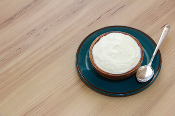 Natural white fermented milk yogurt in a wooden plate next to a metal spoon