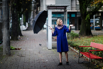 A woman with an umbrella is the street checking for rain.