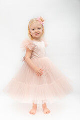 Little barefoot girl smiles wears pink dress with satin skirt. Happy little child in festive outfit isolated on white background. Vertical frame