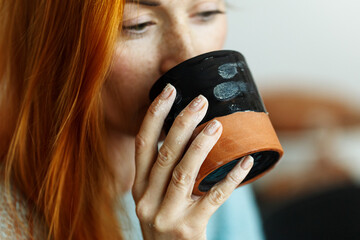 Caucasian woman potter enjoy drinking hot tea from handicraft mug in creative studio of ceramic art. Successful handmade pottery workshop owner refreshing with drink between master classes