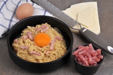 Assiette de spaghetti à la carbonara avec un jaune d'oeuf et ses ingrédients