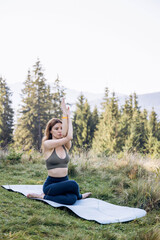 Flexible girl doing yoga in the mountains among the fir trees on a sunny day.