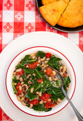 Overhead view of vegan black eye peas and collard greens with corn bread on a red checked table cloth