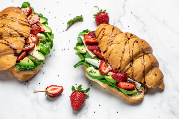 Croissant sandwich with avocado, strawberries, brie camembert cheese, fresh salad sprinkled with...