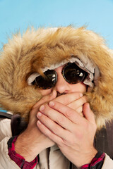 Closeup portrait of bearded man in sunglasses close his mouth with hands over blue background. Concept of emotions, facial expression, sport