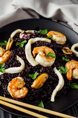 delicious black rice with shrimps and seafood on a black wooden rustic background