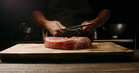 Chef sharpening his knife in front of kitchen table. Cooker preparing his tools before cutting raw meat