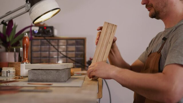 Leathersmith installs tool on workbench surface to process leather in workshop closeup. Master crafts original accessories from natural leather material