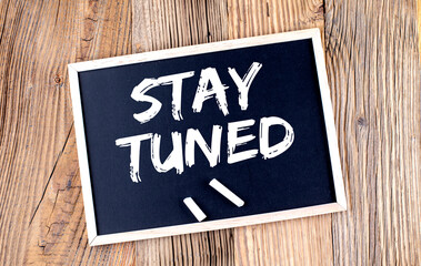 STAY TUNED text on a chalkboard on the wooden background