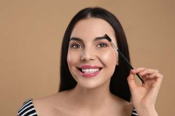 Fototapeta premium Happy woman applying makeup with eyebrow brush on light brown background