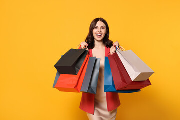 Beautiful young woman with paper shopping bags on yellow background
