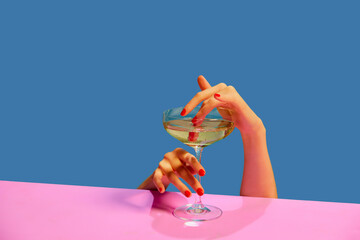 Female hands holding glass with champagne over blue pink background. Food pop art