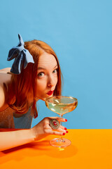 Stylish young woman with festive makeup sipping champagne over yellow blue background. Party mood