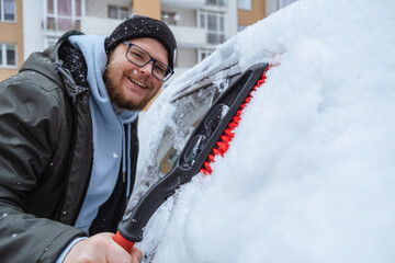 A man is cleaning a car that has been covered in snow - obrazy, fototapety, plakaty