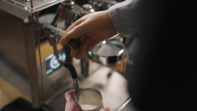 Disabled man with silicone prosthesis hand, barista without arm working in cafe steaming milk in coffee machine pitcher. Physical disability people at work, inclusion and inclusiveness concept