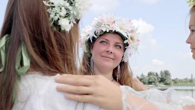 Slow motion smiling faces of young women in traditional shirts and flower wreaths who dance in a round dance. Slavic Feast of Ivan Kupala